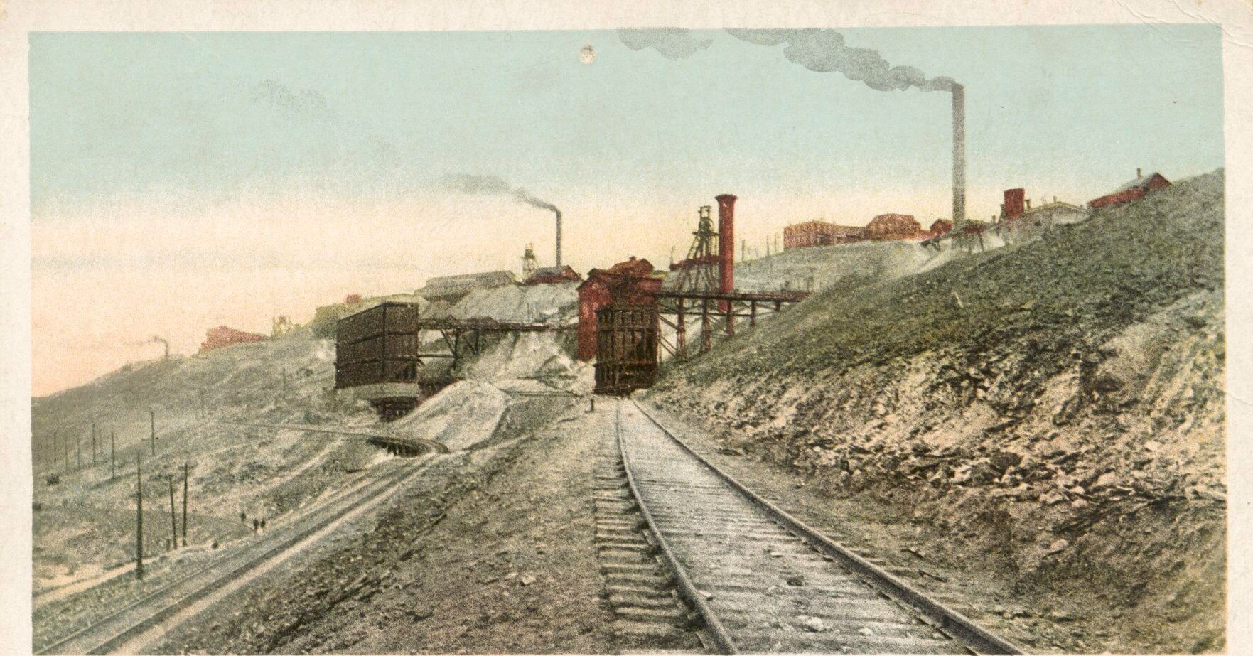 Postcard view of the Anaconda Mine in Butte with rail tracks curving past ore buildings and smokestacks